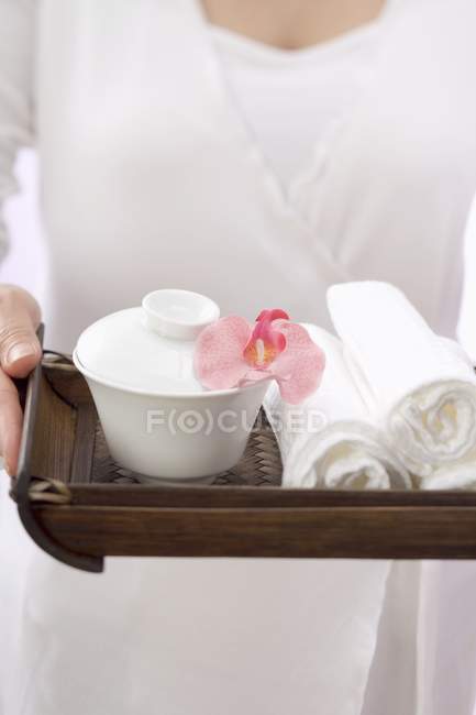 Mulher segurando toalhas com tigela e orquídea na bandeja — Fotografia de Stock