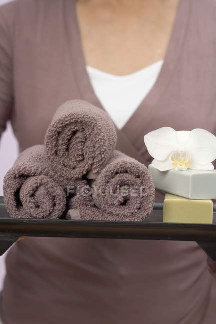 Mujer sosteniendo toallas, jabones y orquídeas en bandeja - foto de stock