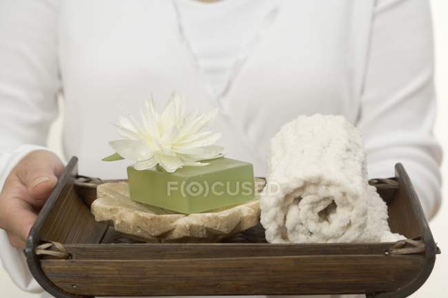Vista de cerca de la mujer sosteniendo jabón, lirio de agua y toalla en la bandeja - foto de stock