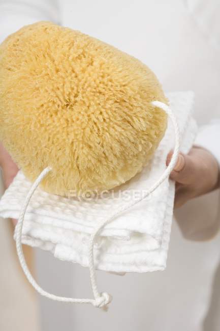Hands holding bath sponge on white towel — Stock Photo