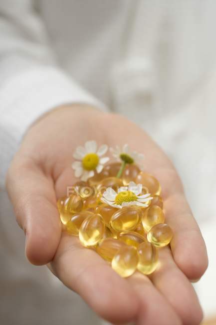 Hand holding vitamin capsules and chamomile flowers — Stock Photo