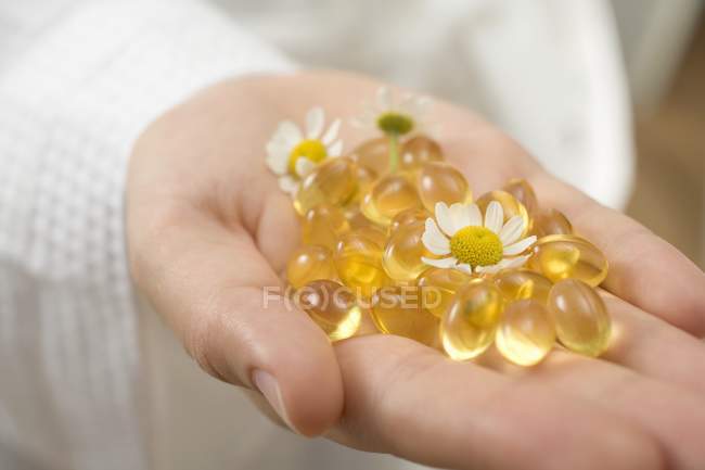 Hand hält Vitaminkapseln und Kamillenblüten — Stockfoto