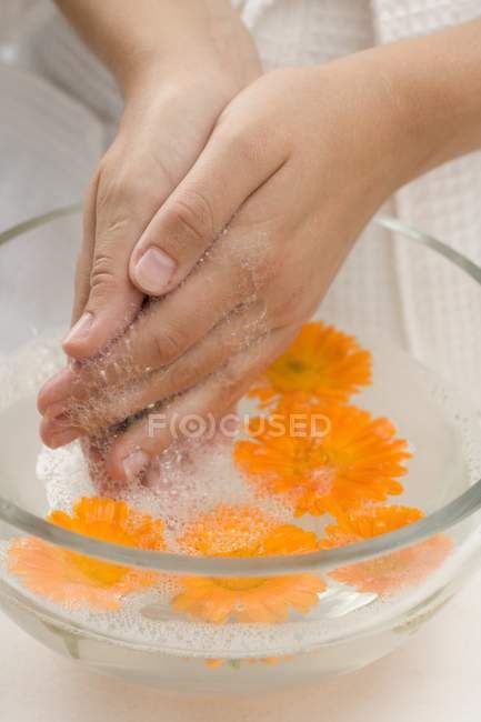 Woman washing hands in soapy water with marigolds — Stock Photo