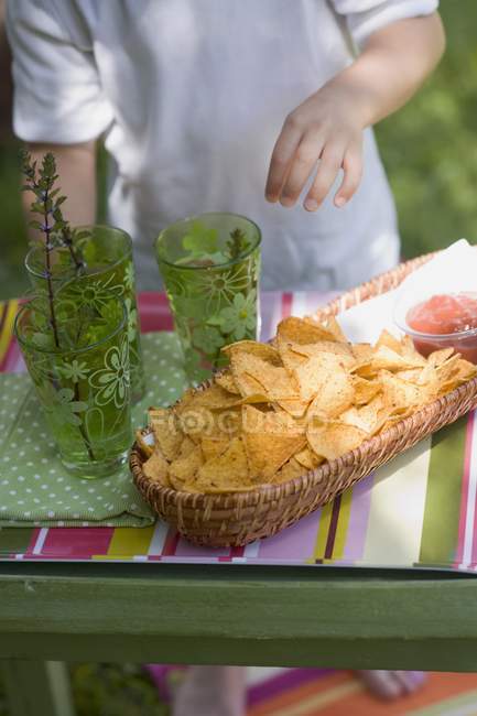 Closeup view of Tortilla chips, salsa and drinks with child on background — Stock Photo