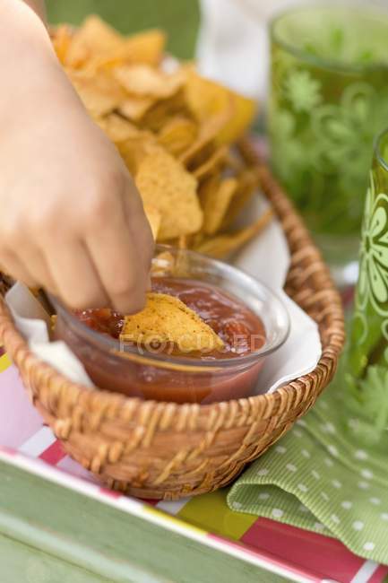 Nahaufnahme der Hand, die Tortilla-Chips in Salsa taucht — Stockfoto