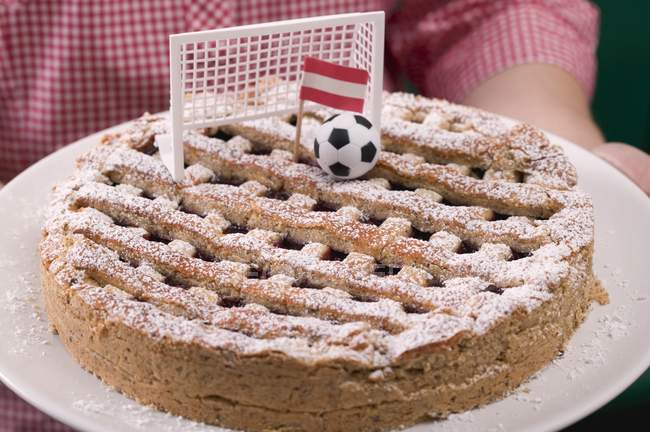 Primer plano vista recortada de la persona que sostiene Linzer torte con fútbol, gol y bandera austriaca - foto de stock