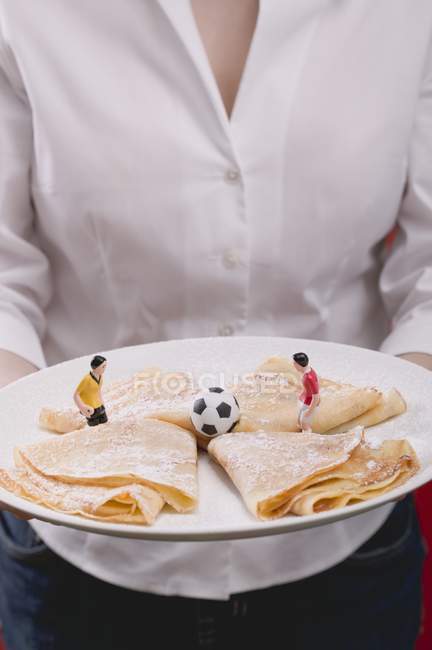 Vista recortada de la mujer sirviendo plato de crepes dulces con figuras de fútbol - foto de stock