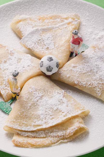 Vista de primer plano de crepes con azúcar glaseado, figuras de fútbol y fútbol - foto de stock