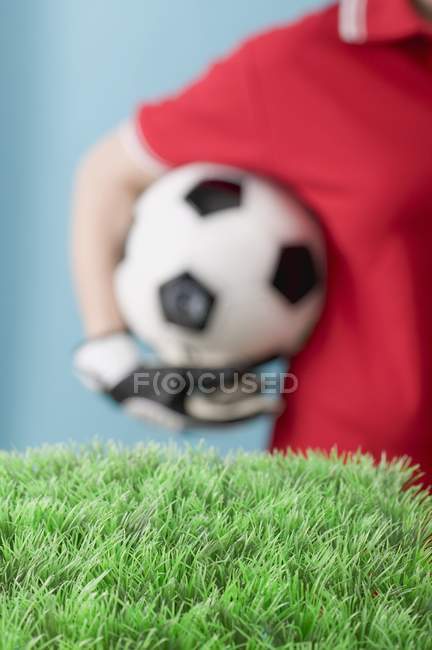 Vista recortada del hombre sosteniendo el fútbol detrás de césped artificial - foto de stock