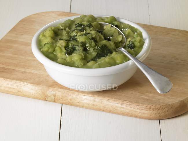 Mushy peas with mint sauce on white plate with spoon on wooden desk — Stock Photo
