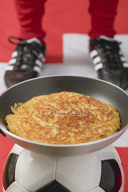 Rsti in frying pan on football, footballer in background — Stock Photo