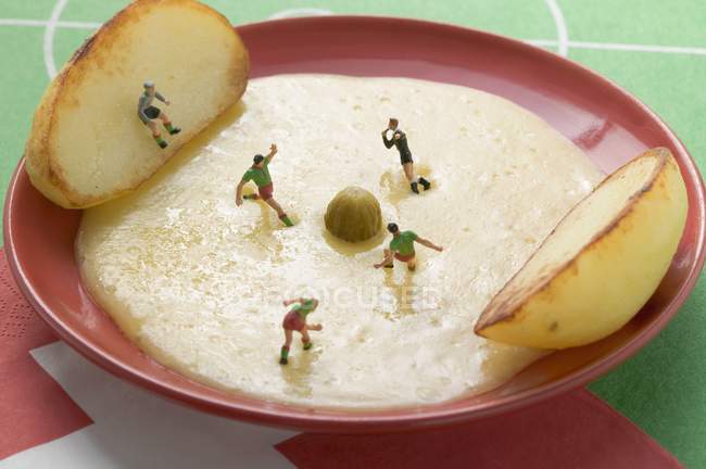 Raclette con patatas, pepinillos y futbolistas de juguete en plato rojo - foto de stock