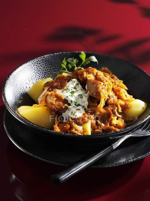 Szeged turkey goulash on potatoes on black plate — Stock Photo
