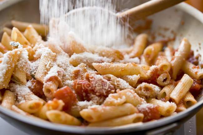 Adding parmesan cheese to penne pasta — Stock Photo