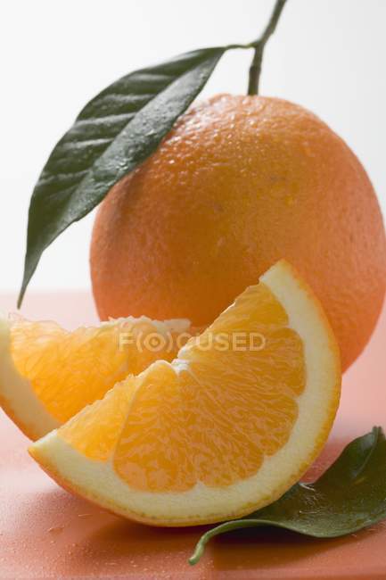 Naranja con cuñas y hojas - foto de stock