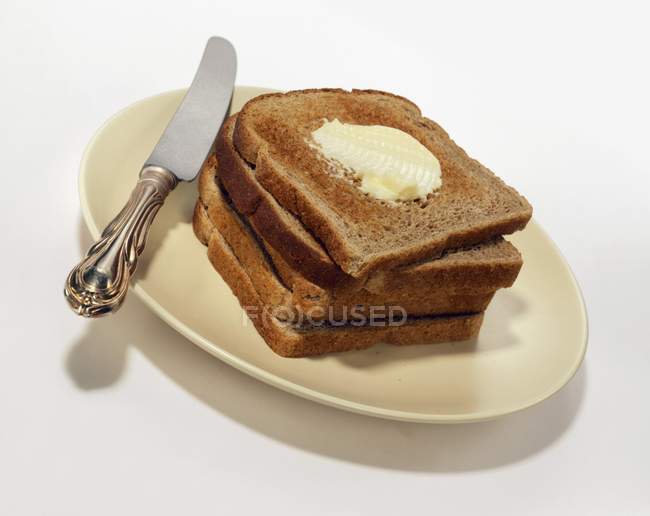 Closeup view of stacked toasts with butter on plate with knife — Stock Photo
