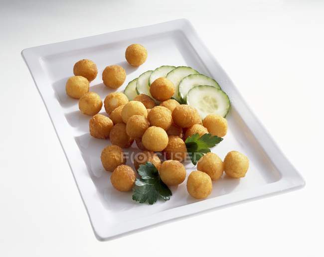 Deep-fried potato balls with sliced cucumber on white plate — Stock Photo
