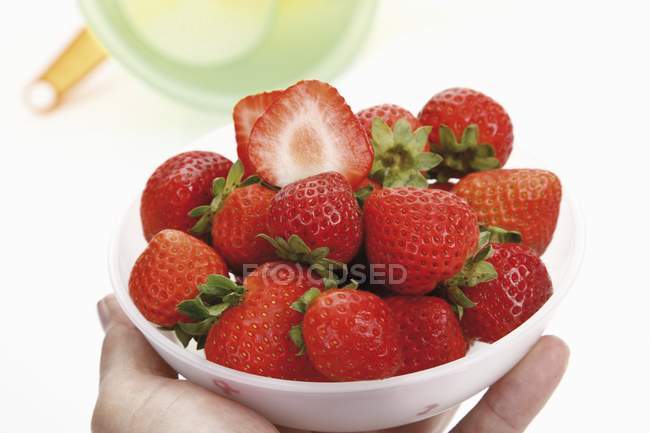 Hand holding strawberries in bowl — Stock Photo