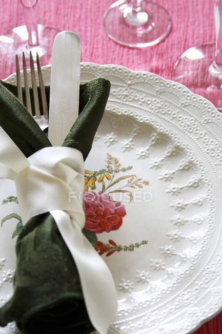Vista close-up de configuração de lugar com faca e garfo envolto em guardanapo e amarrado com fita branca na placa ornamentada — Fotografia de Stock