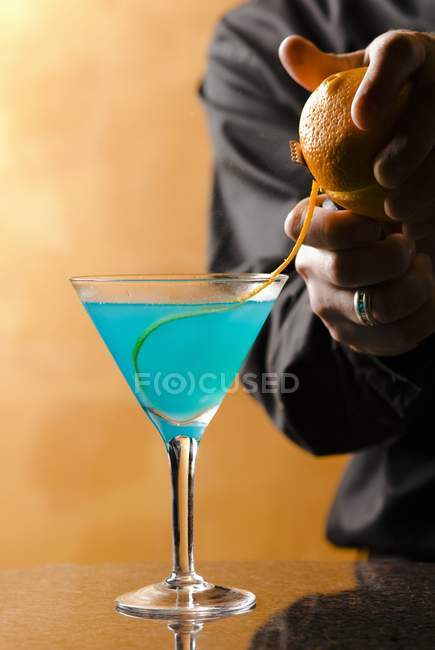 Vista de close-up do bartender adicionando casca de laranja enfeite ao coquetel azul — Fotografia de Stock