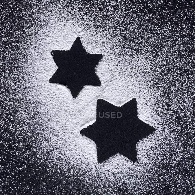 Top view of star shapes in icing sugar on black surface — Stock Photo