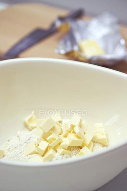 Vue rapprochée des morceaux de beurre sur la farine dans un bol blanc — Photo de stock