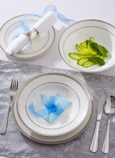 Place-setting with pickled gherkins in a dish over table with plates and towel — Stock Photo