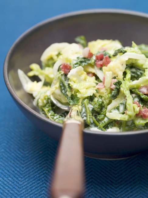 Savoy cabbage with bacon in saucepan over blue surface — Stock Photo