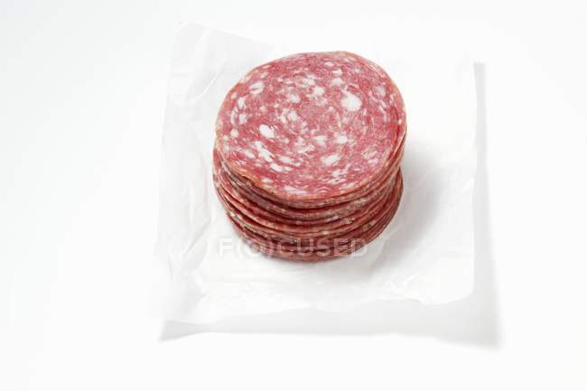 Вид крупным планом наваленных ломтиков свиной колбасы на белой бумаге — стоковое фото