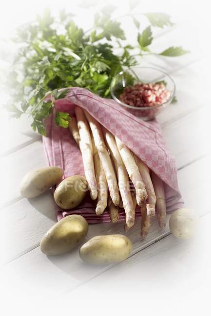 White asparagus in tea towel, potatoes, parsley on wooden surface — Stock Photo