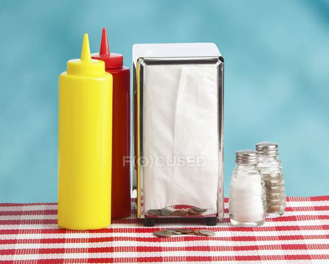 Старомодный стол с кетчупом и горчичными бутылками, салфетками, монетами и кастерами специй — стоковое фото