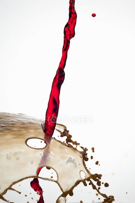 Vue rapprochée de la croisade versant une boisson rouge avec éclaboussures brunes sur fond blanc — Photo de stock