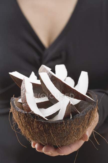 Крупный план женщины, держащей кусочки кокоса в выдолбленном кокосе — стоковое фото