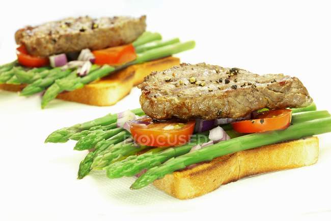 Toasts with asparagus and steaks — Stock Photo