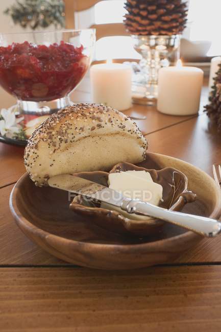 Rollo de semillas de amapola con mantequilla y cuchillo en mesa decorada - foto de stock