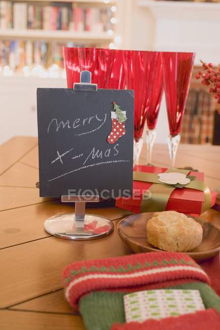 Merry X-mas writing on black board near glasses and place setting on table by fireplace — Stock Photo