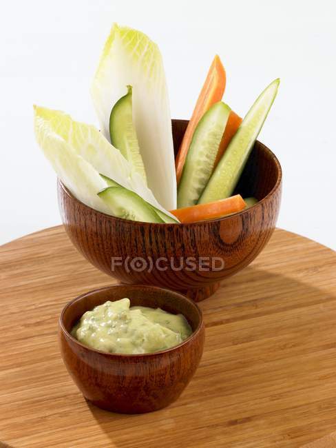 Сырые овощи в мисках с соусом авокадо на деревянной поверхности — стоковое фото