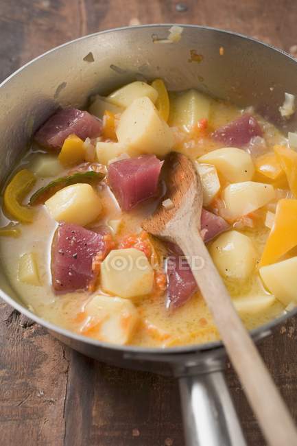 Картофельное и овощное рагу с тунцом в металлической сковороде с деревянной ложкой — стоковое фото
