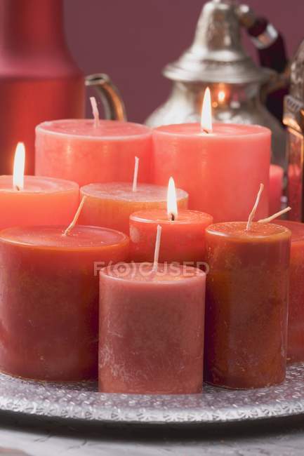 Vista de cerca de varias velas rojas en la bandeja y tetera en el fondo - foto de stock
