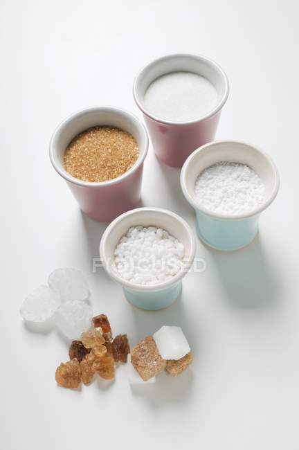 Vari tipi di zucchero in berretti e su superficie bianca — Foto stock