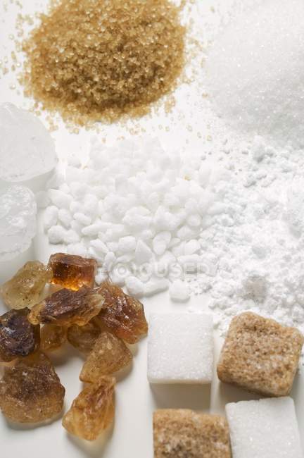 Vista close-up de vários tipos de açúcar na superfície branca — Fotografia de Stock