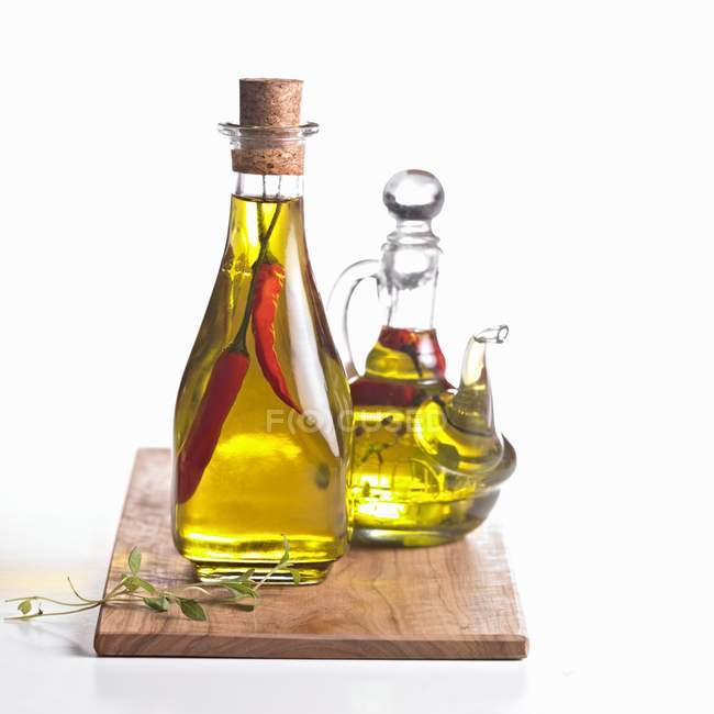 Olio di peperoncino e con erbe aromatiche in due caraffe di vetro su tavola di legno — Foto stock