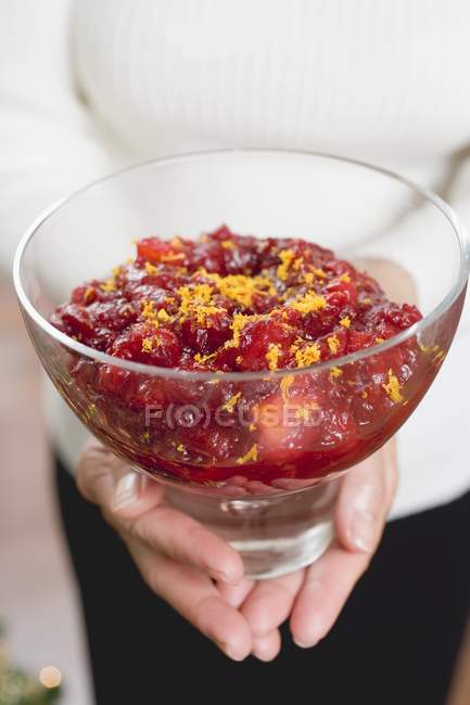 Closeup cropped view of person holding cranberry sauce with orange zest in glass bowl — Stock Photo