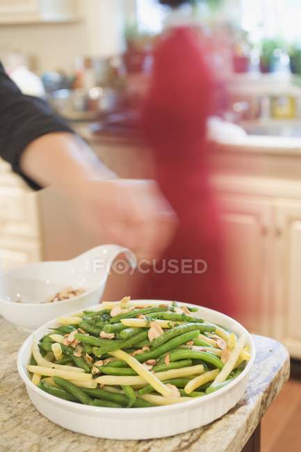 Hand scattering flaked almonds on beans, woman in background — Stock Photo