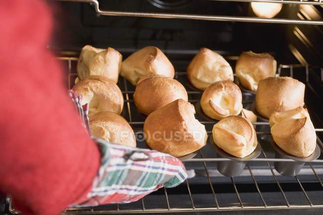 Vista ritagliata di mano prendendo popovers appena sfornati fuori dal forno — Foto stock