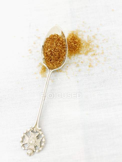 Closeup view of Demerara sugar on silver spoon and on white surface — Stock Photo