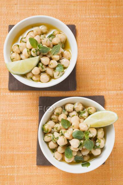 Chick-peas with lime wedges and herbs on white plates — Stock Photo