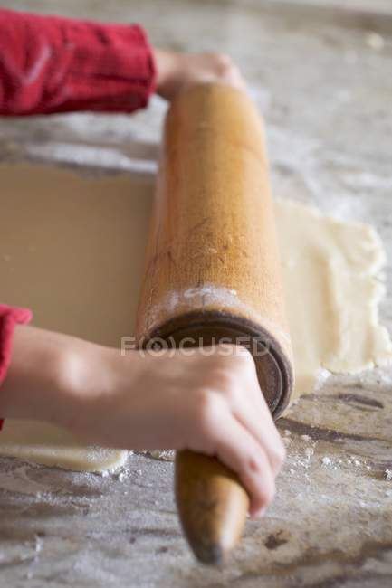 Vue rapprochée des mains de l'enfant déroulant la pâte de biscuit — Photo de stock