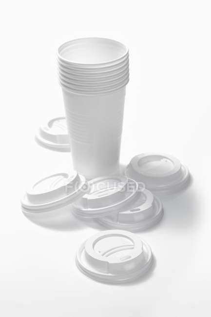 Vista sopraelevata di tazze di caffè impilati in plastica con tappi sulla superficie bianca — Foto stock
