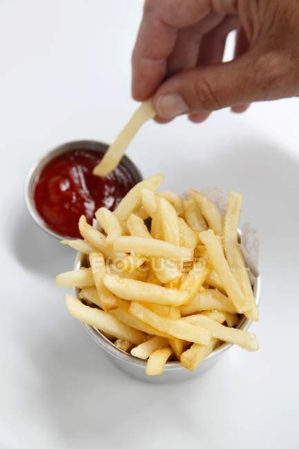 Mão mergulhando batata frita em ketchup — Fotografia de Stock